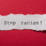 closeup of white torn paper text saying 'stop racism!' on red paper background