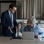 Annoyed young male employee argue with nervous old age colleague