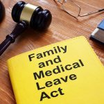 Gavel, glasses, and a book titled "Family and Medical Leave Act" on a wooden surface.