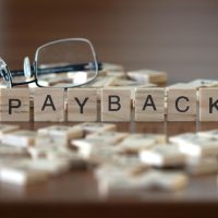 payback word or concept represented by wooden letter tiles on a wooden table with glasses and a book